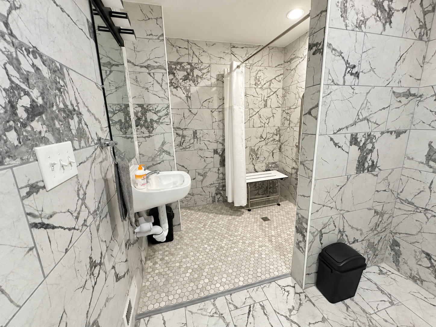 Accessible zero-threshold roll-in shower with marble tile, bench, and grab bars